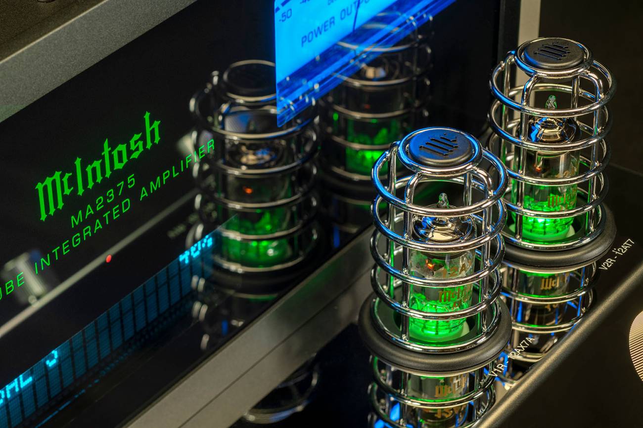 Gros plan sur les tubes du préamplificateur du McIntosh MA2375 sous leurs cages chromées avec éclairage vert, étiquettes 12AX7A et 12AT7 visibles, à côté du logo vert McIntosh MA2375 Tube Integrated Amplifier et d'un vumètre bleu