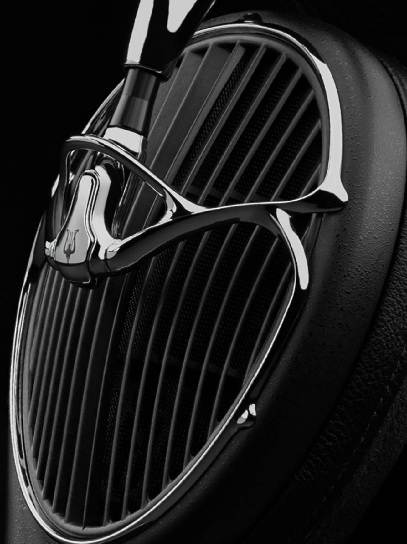 Gros plan sur une coque du casque Meze Audio ARTA montrant le cadre sculptural en métal chromé poli orné du logo trident Meze, la grille à lames acoustiques avec sa maille interne et le coussinet en cuir noir