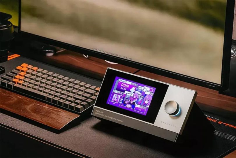 Le DAC ampli casque de bureau Muse HiFi Muse 300 en finition aluminium posé sur un bureau, écran 5 pouces affichant le thème ACG anime, molette de volume à droite, à côté d'un clavier mécanique
