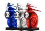 Trois enceintes Bowers & Wilkins Nautilus en finition peinture sur mesure bleu, blanc et rouge, posées sur socles granit noir, dévoilant leur spirale de grave enroulée et leurs tubes effilés de médium et d'aigu