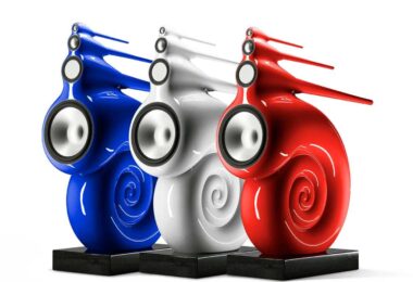 Trois enceintes Bowers & Wilkins Nautilus en finition peinture sur mesure bleu, blanc et rouge, posées sur socles granit noir, dévoilant leur spirale de grave enroulée et leurs tubes effilés de médium et d'aigu
