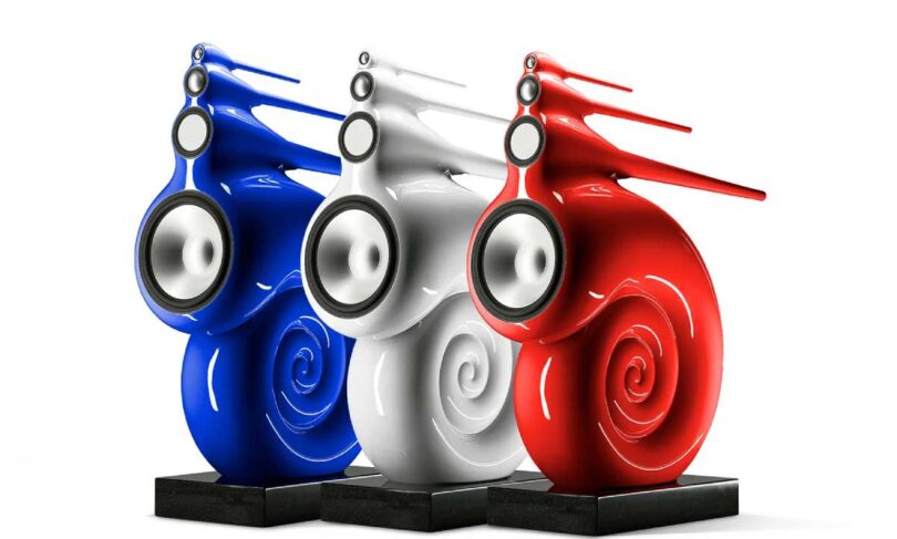 Trois enceintes Bowers & Wilkins Nautilus en finition peinture sur mesure bleu, blanc et rouge, posées sur socles granit noir, dévoilant leur spirale de grave enroulée et leurs tubes effilés de médium et d'aigu