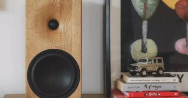 Enceinte bibliothèque Buchardt Audio E50-S en finition chêne naturel massif arrondi, posée sur un meuble bas en bois clair, montrant le tweeter dôme textile Scan-Speak encastré dans son guide d'ondes usiné et le woofer Satori TeXtreme 7,5 pouces à cône noir