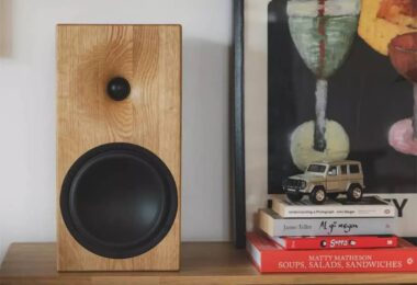 Enceinte bibliothèque Buchardt Audio E50-S en finition chêne naturel massif arrondi, posée sur un meuble bas en bois clair, montrant le tweeter dôme textile Scan-Speak encastré dans son guide d'ondes usiné et le woofer Satori TeXtreme 7,5 pouces à cône noir