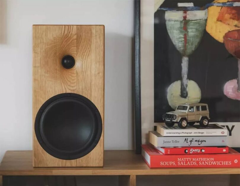 Enceinte bibliothèque Buchardt Audio E50-S en finition chêne naturel massif arrondi, posée sur un meuble bas en bois clair, montrant le tweeter dôme textile Scan-Speak encastré dans son guide d'ondes usiné et le woofer Satori TeXtreme 7,5 pouces à cône noir