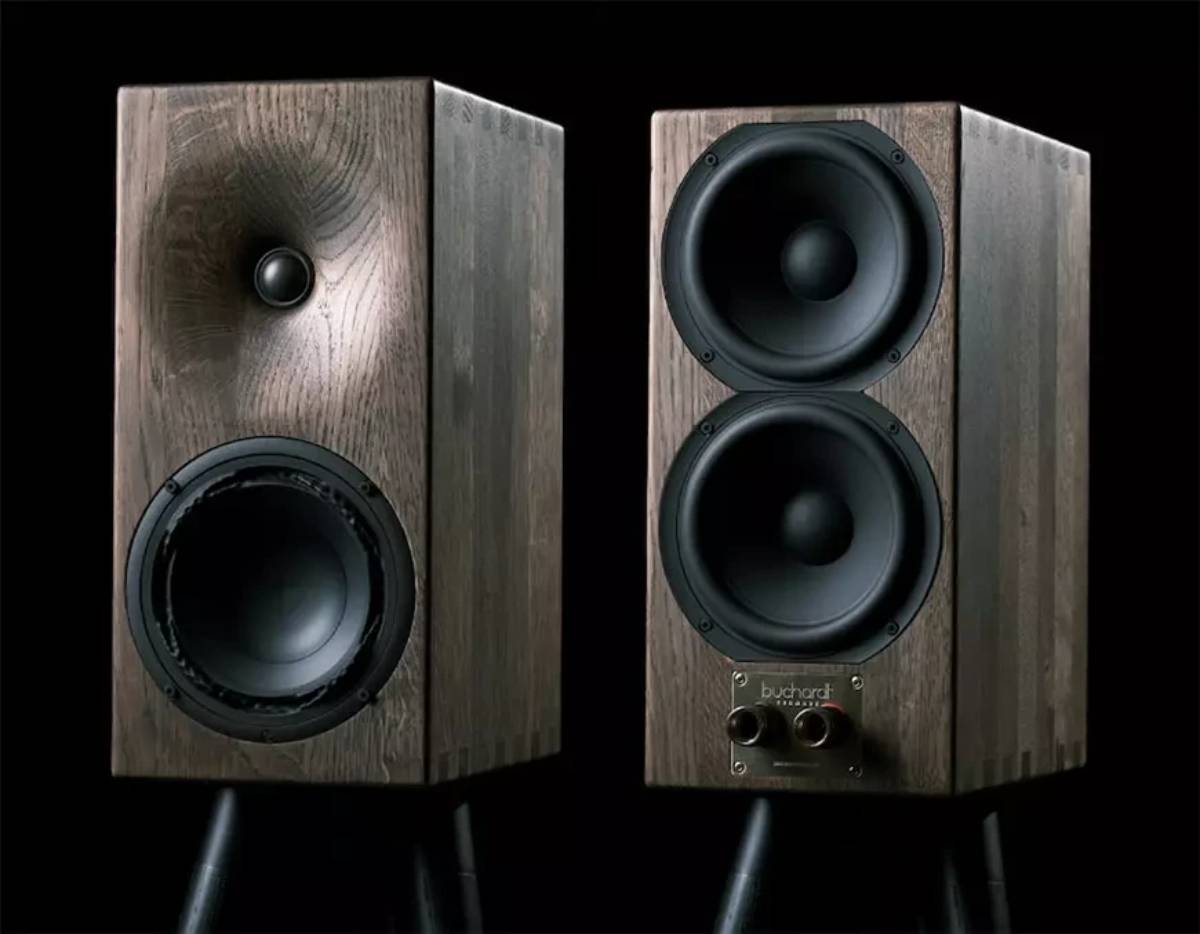 Paire d'enceintes Buchardt Audio E50-S en finition chêne foncé sur fond noir, l'enceinte de gauche vue de face avec son tweeter dôme dans le guide d'ondes et son woofer Satori TeXtreme, celle de droite vue de dos montrant les deux radiateurs passifs de 6 pouces empilés verticalement au-dessus de la plaque signature Buchardt et du bornier