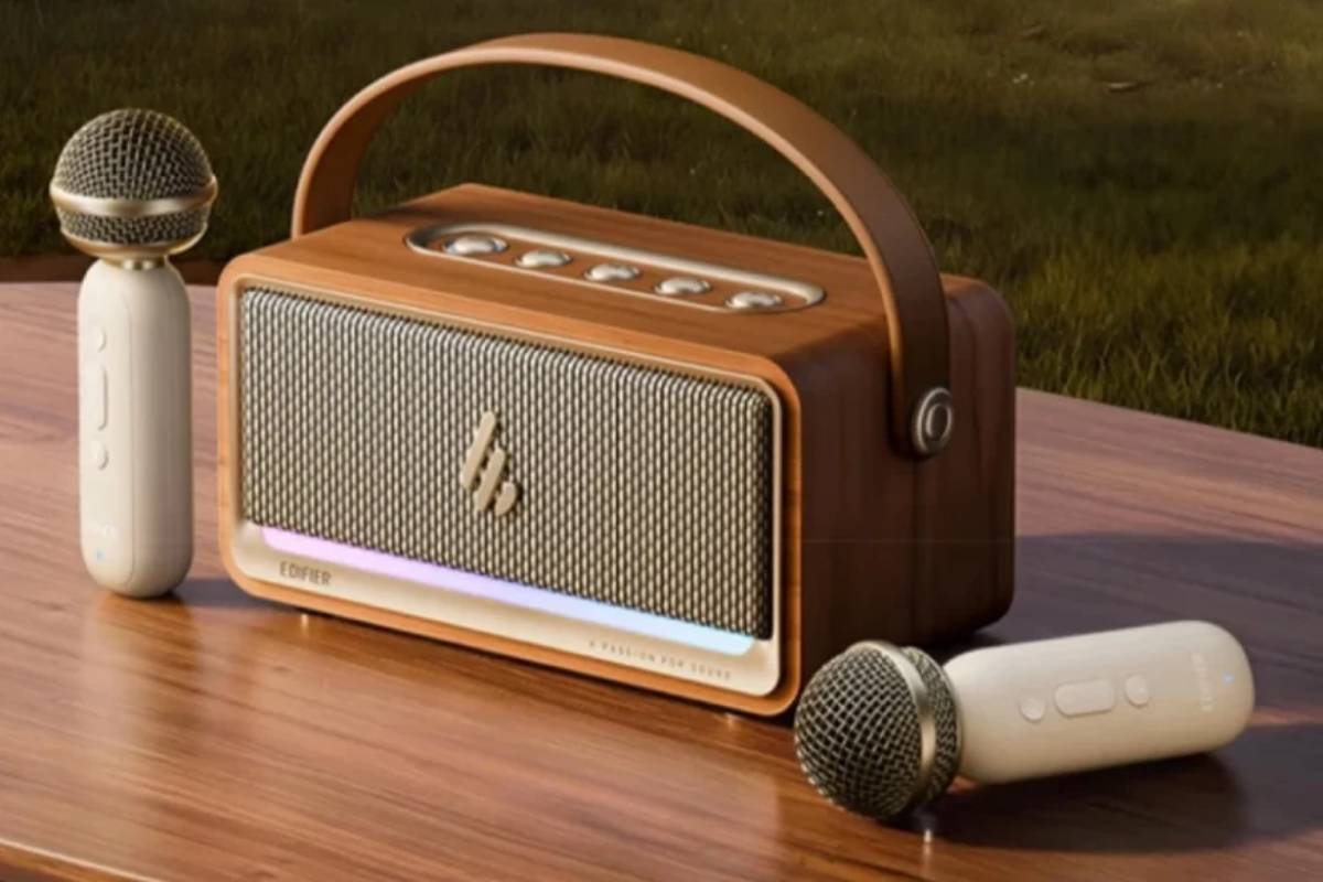Enceinte karaoké Edifier K200 en finition bois posée sur une table en bois à l'extérieur, vue de trois quarts, encadrée par ses deux micros sans fil ivoire à grille dorée, bandeau LED rose et blanc allumé en bas de façade et poignée cintrée en similicuir brun relevée