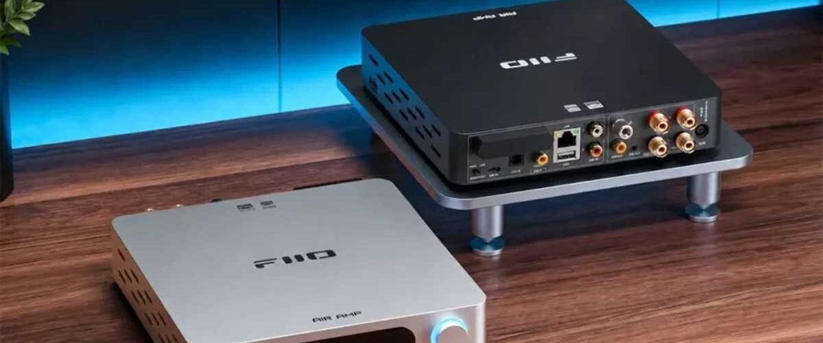 Deux amplificateurs de streaming FiiO Air Amp sur un bureau en bois : au premier plan la version argent vue de face avec son écran LCD affichant le mode STREAM et ses deux molettes rétroéclairées volume et treble, en arrière-plan la version noire vue de dos montrant le port Ethernet, les entrées USB, coaxiale et optique, les RCA Line In et le bornier haut-parleurs