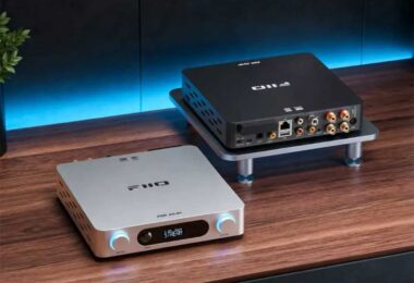 Deux amplificateurs de streaming FiiO Air Amp sur un bureau en bois : au premier plan la version argent vue de face avec son écran LCD affichant le mode STREAM et ses deux molettes rétroéclairées volume et treble, en arrière-plan la version noire vue de dos montrant le port Ethernet, les entrées USB, coaxiale et optique, les RCA Line In et le bornier haut-parleurs