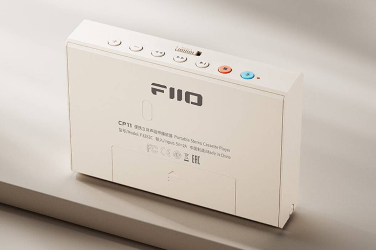 Face arrière du lecteur de cassettes portable FiiO CP11 en coloris crème avec logo FIIO, plaque signalétique mentionnant le modèle F3283C et une entrée de charge 5V 2A, marquages de conformité FCC CE WEEE et EAC, large trappe coulissante en partie basse et rangée de boutons de transport avec touche stop orange et touche Bluetooth bleue sur la tranche supérieure