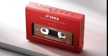 Lecteur de cassettes portable FiiO CP11 en finition rouge vu de trois quarts, fenêtre transparente laissant voir la cassette insérée, rangée de boutons de transport sur la tranche supérieure avec touche Bluetooth bleue et touche orange, connectique sur le flanc droit