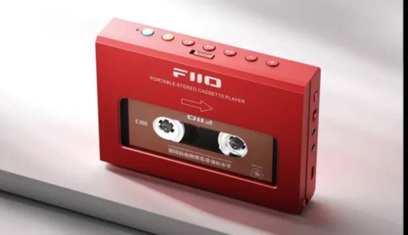 Lecteur de cassettes portable FiiO CP11 en finition rouge vu de trois quarts, fenêtre transparente laissant voir la cassette insérée, rangée de boutons de transport sur la tranche supérieure avec touche Bluetooth bleue et touche orange, connectique sur le flanc droit