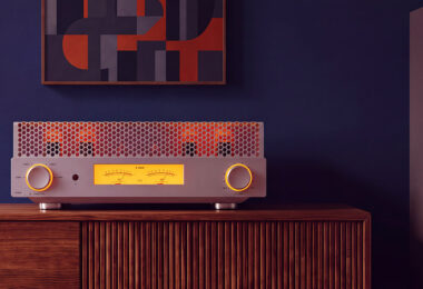 Amplificateur à tubes FiiO EA13 en finition silver posé sur un buffet en bois, capot perforé laissant voir les tubes EL34 incandescents, double vumètre mécanique rétroéclairé ambre et molette de volume à cerclage lumineux