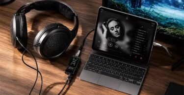 Casque circum-aural ouvert à transducteurs planar magnétiques posé sur un bureau en bois, câble détachable relié à un DAC amplificateur portable à écran affichant 44,1 kHz, lui-même connecté à un ordinateur portable en lecture musicale