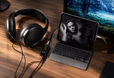 Casque circum-aural ouvert à transducteurs planar magnétiques posé sur un bureau en bois, câble détachable relié à un DAC amplificateur portable à écran affichant 44,1 kHz, lui-même connecté à un ordinateur portable en lecture musicale