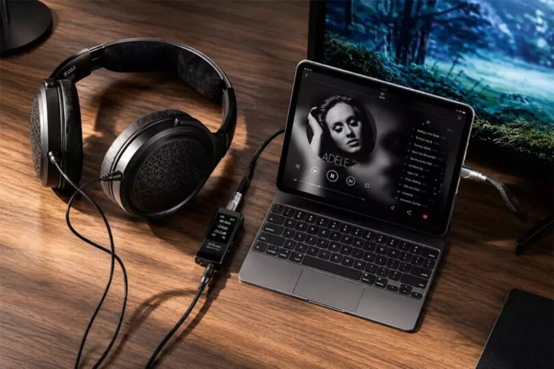 Casque circum-aural ouvert à transducteurs planar magnétiques posé sur un bureau en bois, câble détachable relié à un DAC amplificateur portable à écran affichant 44,1 kHz, lui-même connecté à un ordinateur portable en lecture musicale
