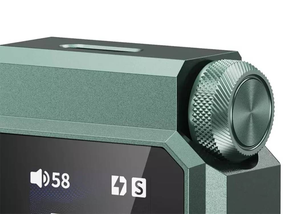 Gros plan sur l'angle supérieur du FiiO QX11 en finition vert foncé, montrant la molette de volume moletée en aluminium usiné, les arêtes chanfreinées du châssis, l'ouverture oblongue de la face supérieure et le haut de l'écran affichant le volume 58
