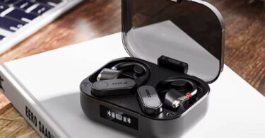 Paire de contours d'oreille Bluetooth FiiO UTWS17 en finition noire posée dans son boîtier de charge à couvercle transparent fumé, écran OLED affichant les niveaux de batterie et l'état d'appairage, connecteurs MMCX rouge et bleu visibles sur les embouts