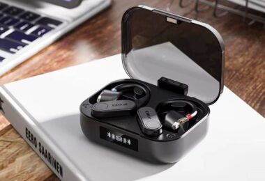 Paire de contours d'oreille Bluetooth FiiO UTWS17 en finition noire posée dans son boîtier de charge à couvercle transparent fumé, écran OLED affichant les niveaux de batterie et l'état d'appairage, connecteurs MMCX rouge et bleu visibles sur les embouts