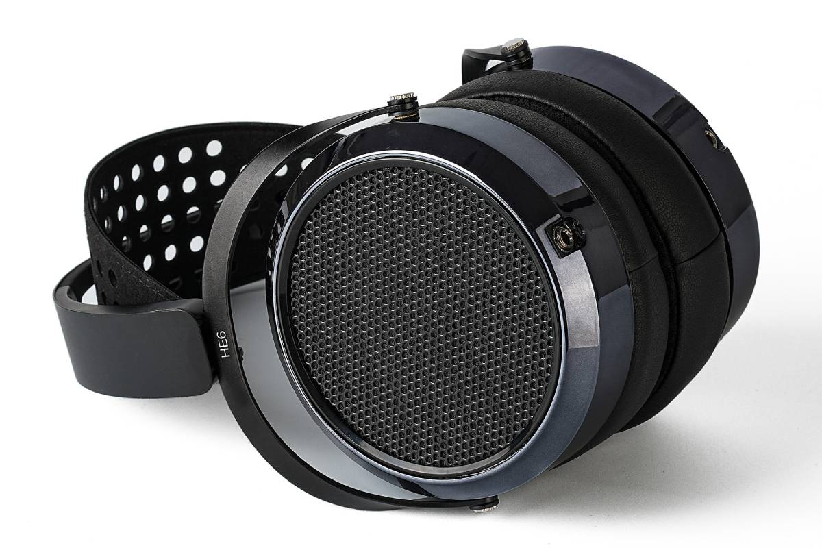 Détail du système de suspension du HIFIMAN HE6 Remastered : bandeau perforé en suédine, fourches rotatives noires, vis moletées de réglage en hauteur, charnières amorties et coussinets épais en cuir protéiné autour de la grille hexagonale du transducteur planaire