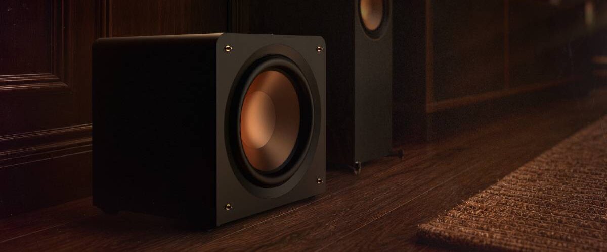 Caisson de basses compact Klipsch RP-1600CSW Reference Premiere à charge close posé au sol près d'une colonne Klipsch, woofer Cerametallic cuivré frontal sans évent, finition vinyle ébène
