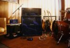 Tête d'ampli Marshall JMH Studio Hendrix 60th Anniversary posée sur un baffle 4x12 recouvert du motif psychédélique violet oil-on-water, avec pédalier assorti au sol, enceinte portable Marshall violette sur une table d'appoint, guitares acoustiques et batterie dans un studio de répétition