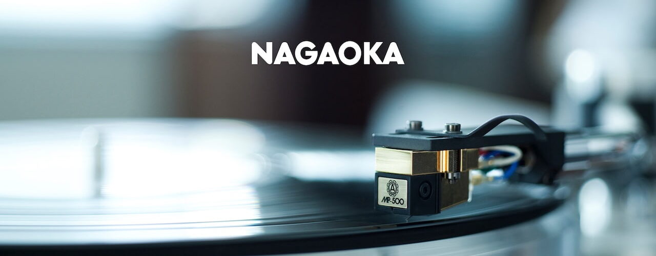 Cellule phono Nagaoka de la série MP vue de trois quarts, corps plastique moulé, cantilever conique en alliage d'aluminium et diamant elliptique visible, avec son diamant de rechange JN-P posé à côté dans son support de protection