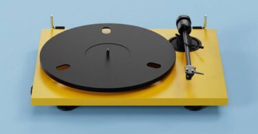 Platine vinyle Pro-Ject E1.2 BT en finition Satin Golden Yellow vue de trois quarts, plateau aluminium noir 730 g, bras aluminium 8,6 pouces avec cellule Pick it MM E et charnières dorées sur fond bleu clair