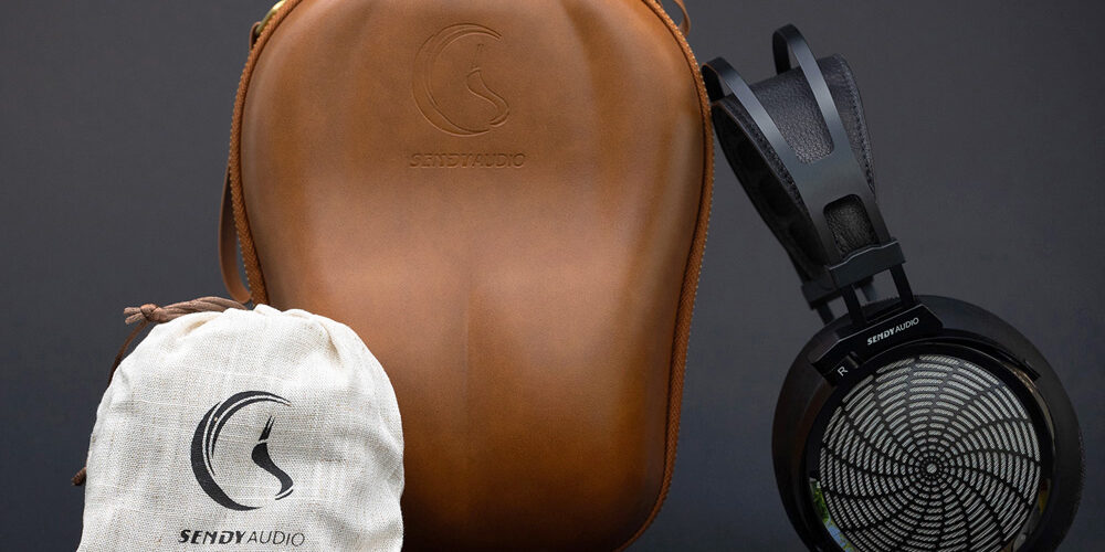 Casque planar magnétique ouvert Sendy Audio Apollo PRO à grille métallique sunburst et arceau noir, présenté avec son étui de transport rigide en cuir marron et sa pochette de rangement en chanvre