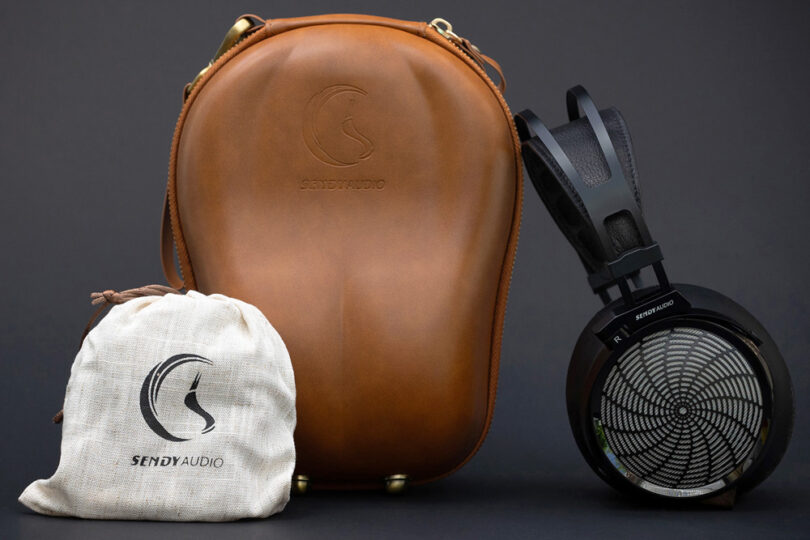 Casque planar magnétique ouvert Sendy Audio Apollo PRO à grille métallique sunburst et arceau noir, présenté avec son étui de transport rigide en cuir marron et sa pochette de rangement en chanvre