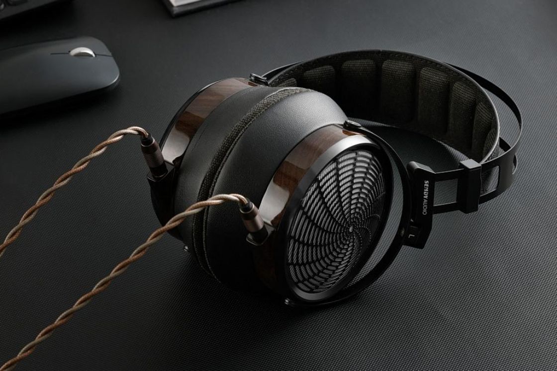 Casque planar magnétique Sendy Audio Apollo PRO posé sur un bureau, coques en zébrano foncé, grille métallique à motif sunburst, arceau noir suspendu et câble détachable double entrée 3,5 mm en cuivre