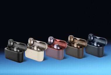 Écouteurs Sennheiser Momentum True Wireless 5 en finition Graphite posés devant leur boîtier de charge Qi au format vertical, avec le transducteur TrueResponse 7 mm et les grilles de microphones visibles sur la face externe des écouteurs