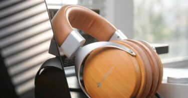 Casque SNOWSKY Nature en finition bois abricot posé sur un bureau près d'une fenêtre, coques circum-aurales fermées à motif bois clair avec logo SNOWSKY, arceau en simili cuir marron, fourches aluminium argenté et double câble détachable 3,5 mm visible