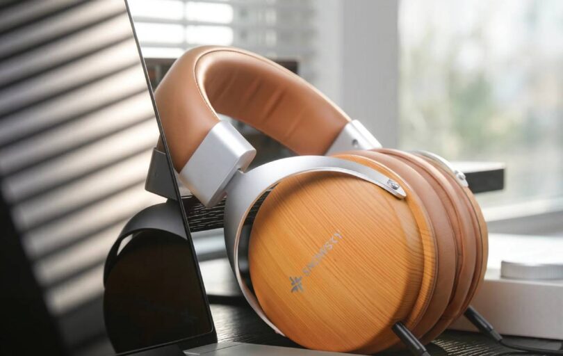 Casque SNOWSKY Nature en finition bois abricot posé sur un bureau près d'une fenêtre, coques circum-aurales fermées à motif bois clair avec logo SNOWSKY, arceau en simili cuir marron, fourches aluminium argenté et double câble détachable 3,5 mm visible
