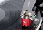 Cellule MC Vertere Ruby One à corps aluminium rouge anodisé montée sous un bras Vertere Groove Runner X, vis de fixation nickelées apparentes, câblage de headshell coloré et pointe diamant en contact avec le sillon d'un disque vinyle noir