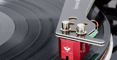Cellule MC Vertere Ruby One à corps aluminium rouge anodisé montée sous un bras Vertere Groove Runner X, vis de fixation nickelées apparentes, câblage de headshell coloré et pointe diamant en contact avec le sillon d'un disque vinyle noir