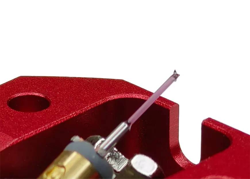 Macro du cantilever télescopique de la cellule Vertere Ruby One montrant la section rubis translucide rosée emmanchée sur la section aluminium, la pointe diamant Micro Ridge à l'extrémité, l'élément doré du générateur et la rondelle d'amortissement, sur corps aluminium rouge sablé