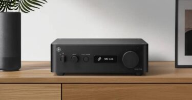 Yamaha WXC-70A en finition noire posé sur un meuble en bois clair, face avant avec interrupteur d'alimentation, sélecteur de source INPUT, touche PLAY/PAUSE, écran affichant MC Link et large molette de volume à droite