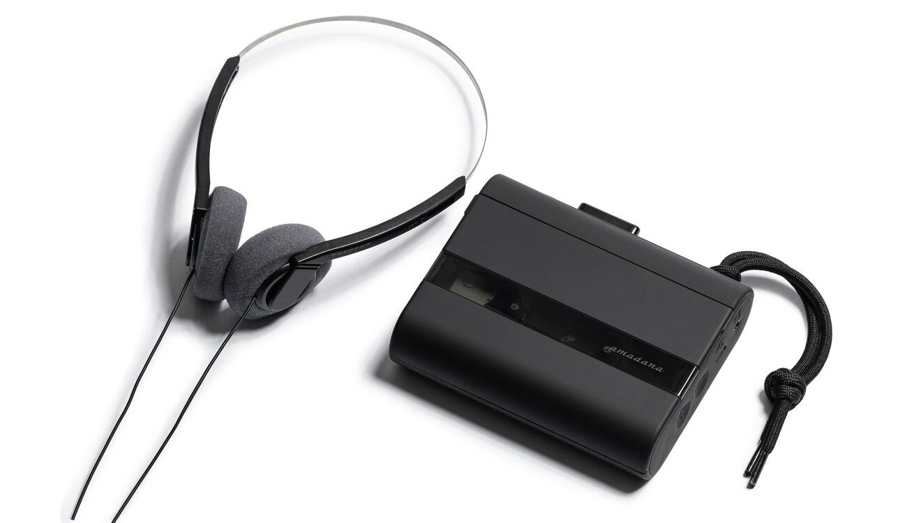 Baladeur cassette Amadana CP10 noir mat avec logo amadana sur le panneau fumé et dragonne tressée, à côté du casque filaire rétro fourni à arceau métallique fin et coussinets en mousse grise, sur fond blanc
