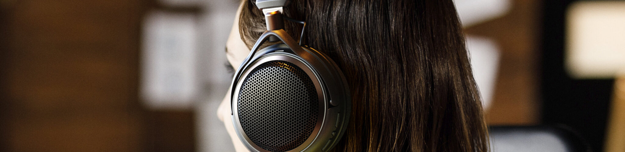 Femme de profil portant le casque ouvert sans fil Audio-Technica ATH-AL5NC, avec grille hexagonale métallique, arceau textile, logo Audio-Technica et accents bronze, dans un intérieur chaleureux