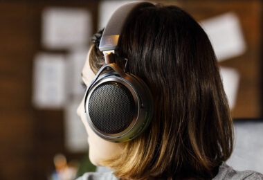 Femme de profil portant le casque ouvert sans fil Audio-Technica ATH-AL5NC, avec grille hexagonale métallique, arceau textile, logo Audio-Technica et accents bronze, dans un intérieur chaleureux