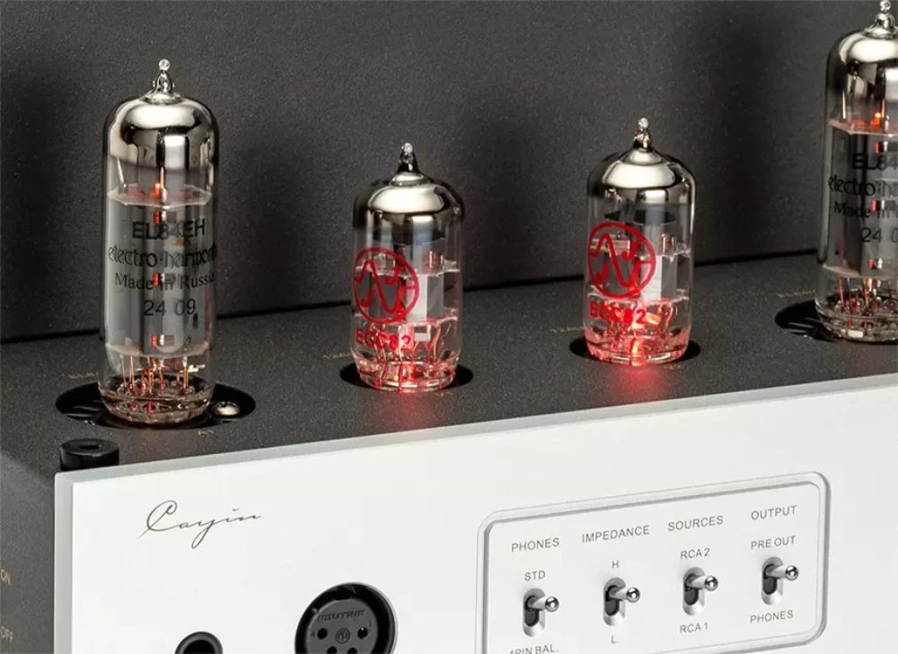 Gros plan sur les lampes du Cayin HA-1A MK3 : deux tubes JJ ECC82 allumés encadrés par deux Electro-Harmonix EL84EH, au-dessus de la façade argent et de ses sélecteurs d'impédance et de source