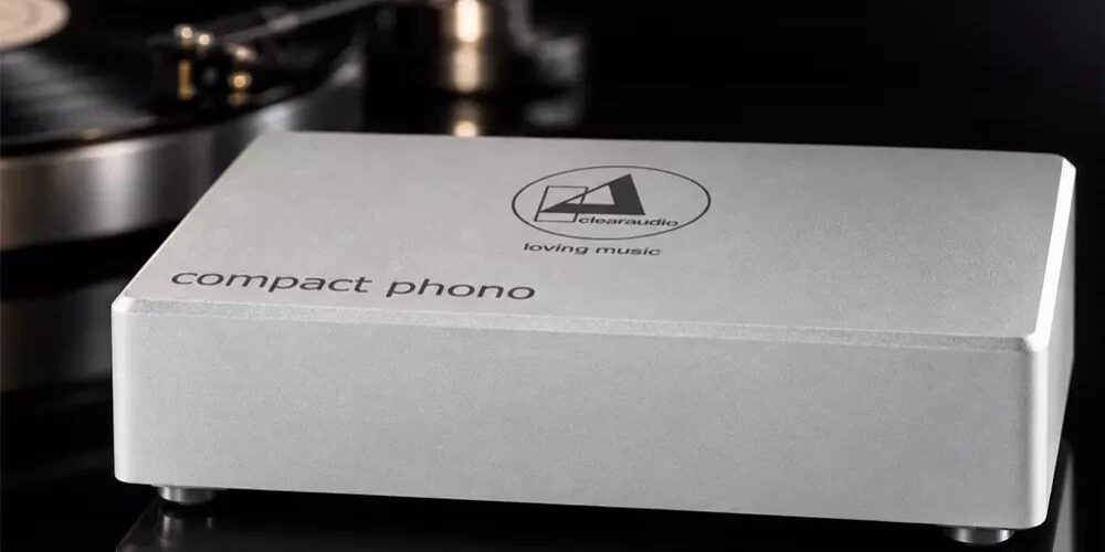 Préampli phono Clearaudio Compact Phono en finition argent, boîtier en aluminium brossé gravé du logo clearaudio loving music et de l'inscription compact phono, posé devant une platine vinyle