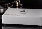 Préampli phono Clearaudio Compact Phono en finition argent, boîtier en aluminium brossé gravé du logo clearaudio loving music et de l'inscription compact phono, posé devant une platine vinyle