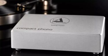 Préampli phono Clearaudio Compact Phono en finition argent, boîtier en aluminium brossé gravé du logo clearaudio loving music et de l'inscription compact phono, posé devant une platine vinyle