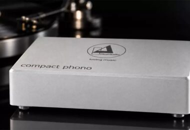 Préampli phono Clearaudio Compact Phono en finition argent, boîtier en aluminium brossé gravé du logo clearaudio loving music et de l'inscription compact phono, posé devant une platine vinyle