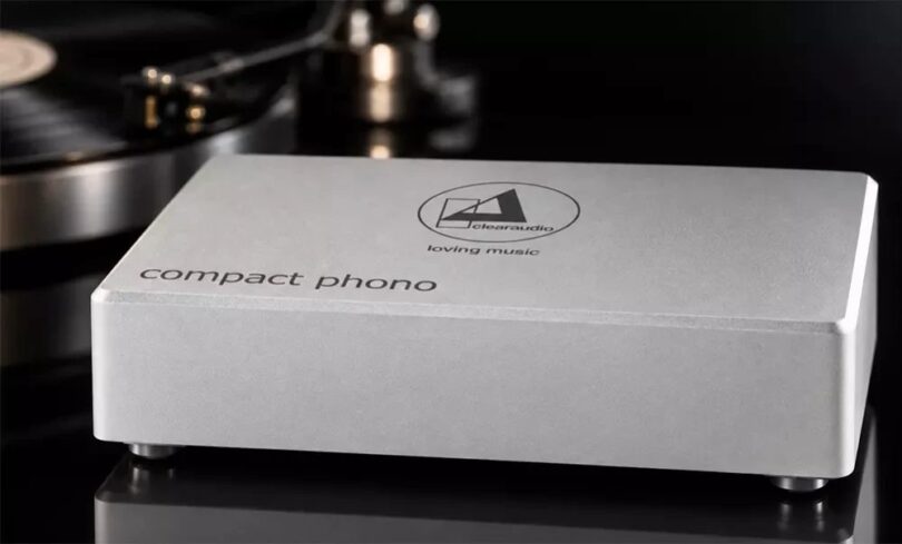 Préampli phono Clearaudio Compact Phono en finition argent, boîtier en aluminium brossé gravé du logo clearaudio loving music et de l'inscription compact phono, posé devant une platine vinyle