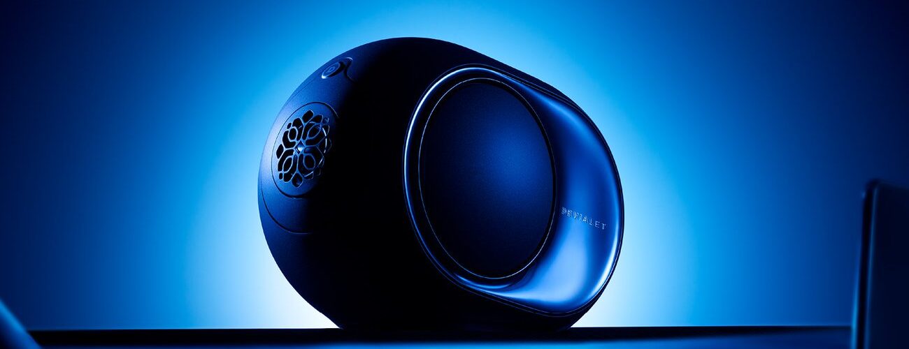 Enceinte connectée Devialet Phantom Ultimate 98 dB Pulse Blue de profil sur fond bleu lumineux, avec flasque latérale miroir, woofer HBI latéral, logo Devialet et commandes tactiles sur le dessus