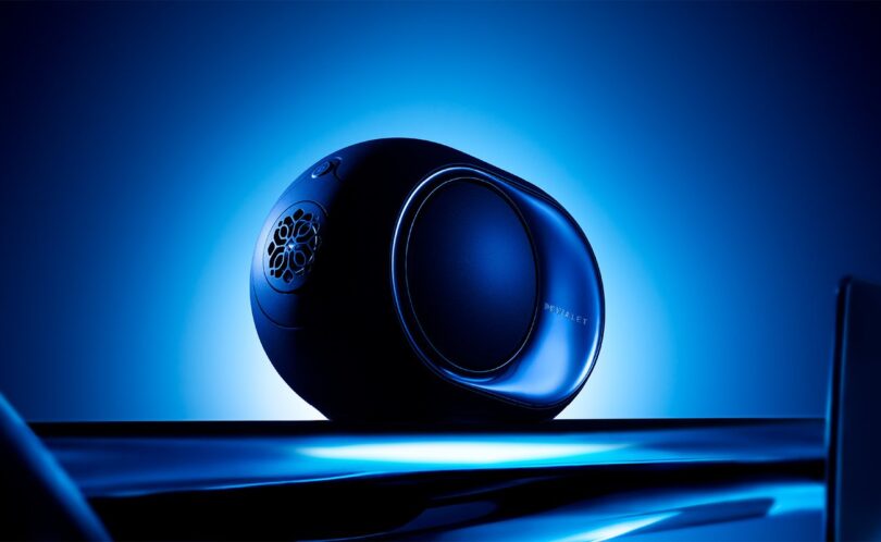 Enceinte connectée Devialet Phantom Ultimate 98 dB Pulse Blue de profil sur fond bleu lumineux, avec flasque latérale miroir, woofer HBI latéral, logo Devialet et commandes tactiles sur le dessus