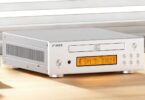 Lecteur CD de bureau FiiO DP11 en finition argent vu de trois quarts, avec tiroir CD frontal logo Compact Disc Digital Audio, écran LCD ambré, boutons de navigation ronds et flancs ajourés en aluminium